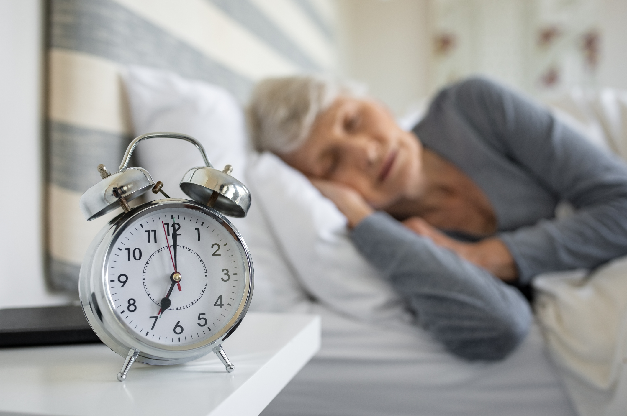 Bien dans mon corps, retraitée qui dort avec un réveil devant elle.