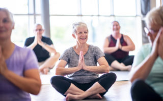 Bien être, bien vieillir, retraitée avec le sourire au qui fait de la meditation assise par terre dans une salle.