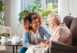 Bien avec mes proches retraitée assise et devant elle il y a une femme qui la regarde et lui tient les main en souriant