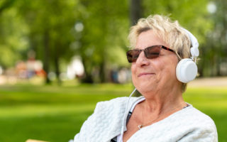 Bien être, bien vieillir, retraitée qui écoute de la musique avec un casque audio dans un parc