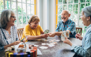 Bien avec les autres, groupe de retraité assis à une table qui rigole et joue aux cartes