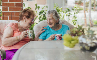 Bien avec les autres, deux retraitées rigolent assises à une table avec une tasse de thé
