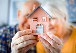 Bien dans mon environnement, un couple de retraités tenant une petite maison dans leurs mains