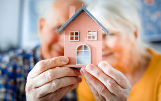 Bien dans mon environnement, un couple de retraités tenant une petite maison dans leurs mains