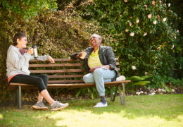 Bien avec les autres, deux retraitées prennent un café et rigolent assises sur un banc