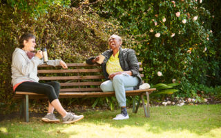 Bien avec les autres, deux retraitées prennent un café et rigolent assises sur un banc