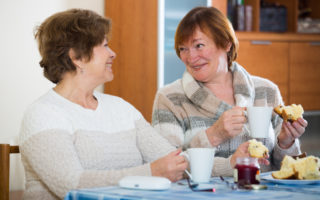 Bien démarrer ma retraite, deux retraitées mangent de la brioche en buvant un café et en rigolant